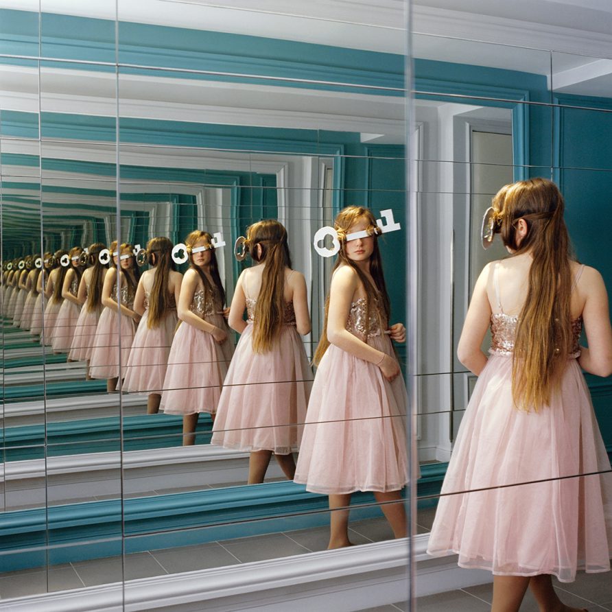 Une fillette aux longs cheveux et aux yeux bandés par une grande clef se reflète à l'infini dans un miroir.