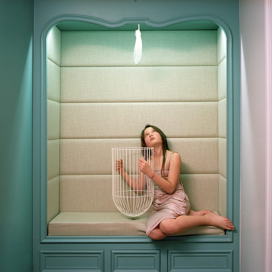 Dans une alcôve, une fillette assise tient une cage à oiseaux à l'envers. Au-dessus de la cage, en haut de l'alcôve se situe une plume blanche.