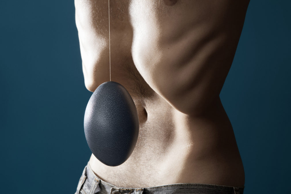 Un ventre d'homme très creusé, créant une cavité. Devant ce creux au ventre plâne, suspendu à un fil, un gros oeuf bleu, un oeuf d'émeu. le fond de l'image est uni et bleu.