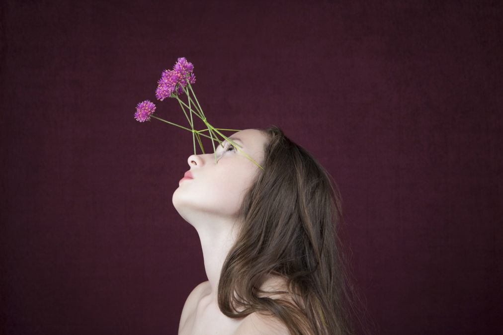 Visage de jeune femme portant comme un appareil oculaire fait de fleurs et leurs tiges, attaché avec un fil à la tête.