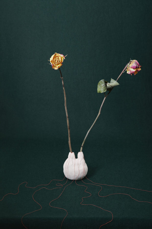 Nature morte. Un vase évoquant un volcan à deux sorties, deux fleurs fanées en sortent; et des fils rouges en coulent, sur un fond vert sombre.